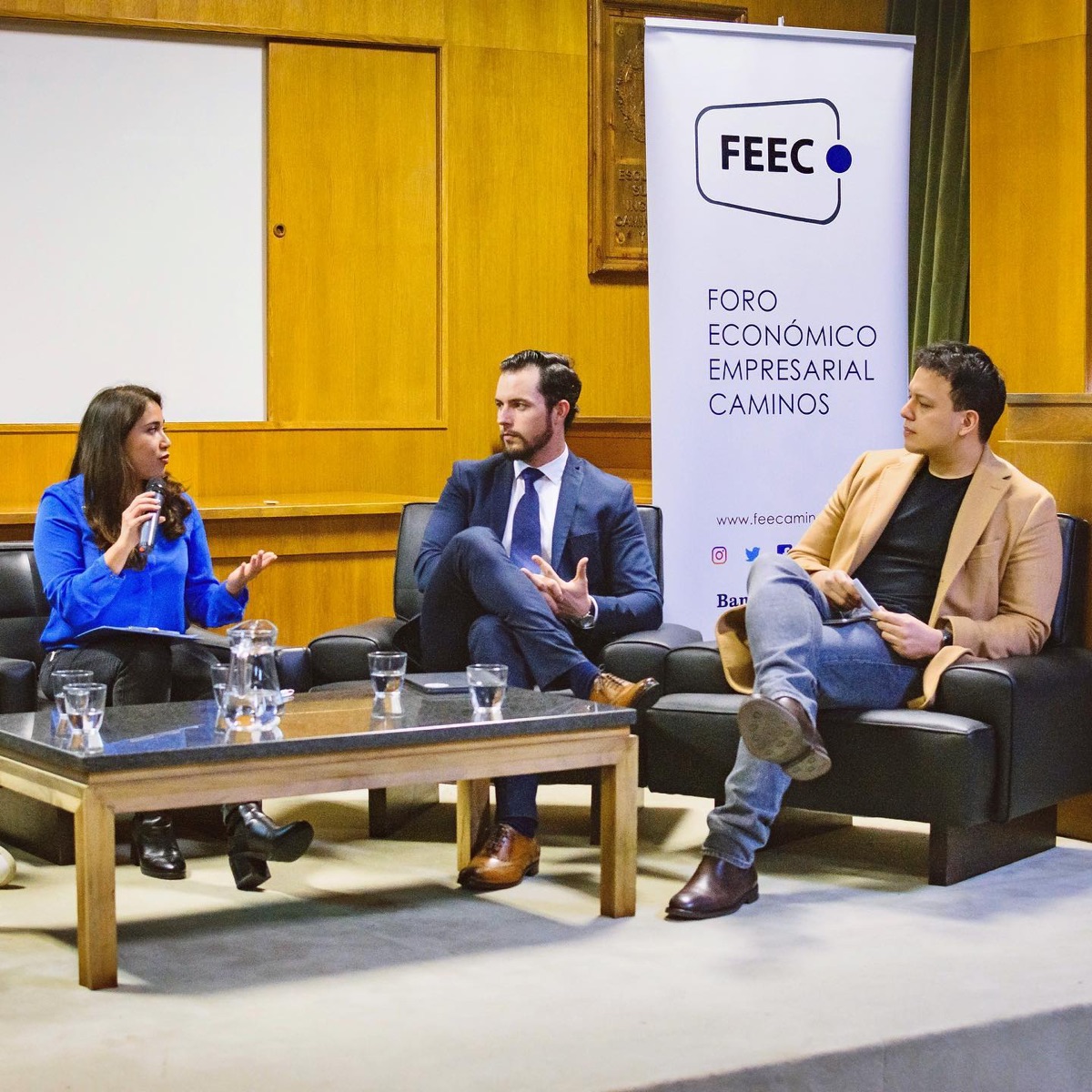 Joshua hablando en un panel de tres personas frente a un cartel de FEEC