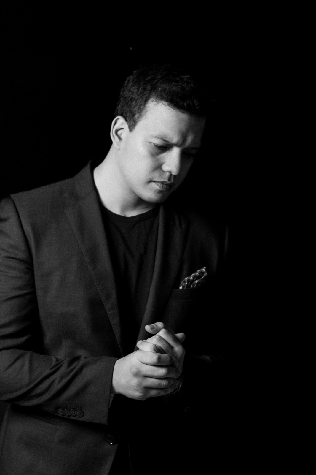 Joshua Ariel in a dark suit, photographed in black and white, hands clasped.